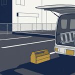 早朝の駐車場。軽バンの荷室に工具箱と脚立が積まれ、地面には空の道具箱が1つ。朝日で長い影が伸びている