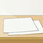 昼過ぎの事務所。明るい木の机の天板の上に、無地の白い紙が2枚だけ少しずらして重ねて置かれている。