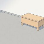 昼どき、誰もいない建物の外階段の下。明るいグレーの土間に、明るい木の四角い踏み台が1つだけ置いてある