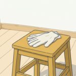 昼の光が入る空室のすみ。明るい木の踏み台の上に、生成り色の布の作業手袋が一組置かれている。手が止まっている昼休みの現場