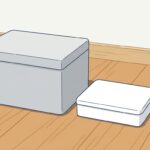 明るい木の床のすみに、ふたを閉じた明るいグレーのクーラーボックスと、真っ白な弁当箱が並んで置かれている。夏の現場に持ち込む昼食と飲み物
