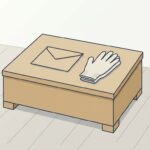 木の低い箱の天面に無地の封筒が1通と、たたんだ布の作業手袋が1組置かれている