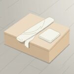 ケガで休んだ日の場面。明るい室内の床に置かれた低い木の箱の天面に、ゆるく巻いた白い布が1本と、たたんだ同じ布が1枚置かれている。巻いた布の端が少しほどけている。