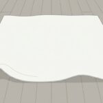 手を止めた現場の場面。明るい室内の床に、生成り色の大きな布が1枚だけ広げて置かれ、手前側の端がゆるく波打って少し持ち上がっている。